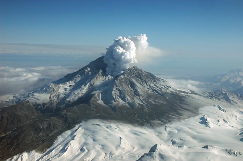 Redoubt Volcano viewed from the northwest following the April 4, 2009 eruption (Event 19).  Steam rises from the summit crater, pyroclastic flow and surge deposits drape the flanks, and lahar deposits cover the Drift River Valley.