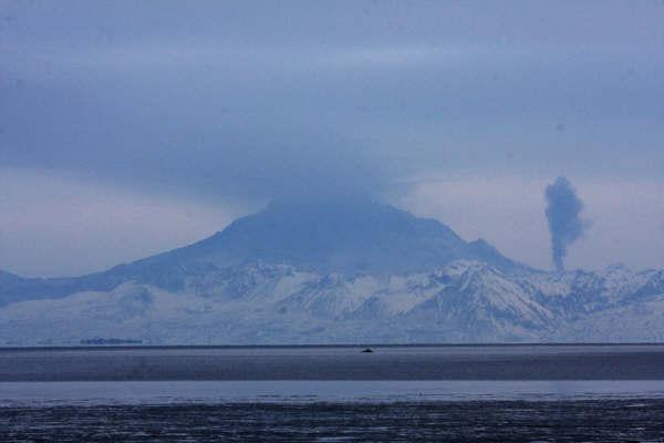 Redoubt Volcano viewed from the east.  The dark, vertical column rising right (north) of the volcano is from a"rootless" phreatic eruption where pyroclastic debris channeled down the Drift glacier during the April 4 eruption overflowed laterally onto a deeply crevassed flank glacier.  The hot debris flowed into several closely spaced crevasses and came in contact with ice creating an intermittent, vigorous steam plume (known informally as "Jr. Plume").      			