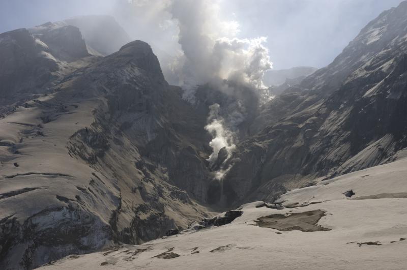 																																														View of the upper gorge from waterfall up to the northern flank of the  active lava dome, Redoubt Volcano. As hot blocks and debris are shed from the dome, small block-and-ash flows are generated (one is visible in this image as a low-lying cloud advancing on the lower slope of the dome.  Hot blocks come to rest in the stream and generate the secondary steam clouds visible between the top of the waterfall and the dome.				