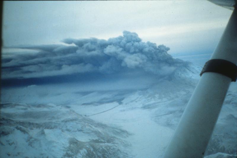 From December 16-19, 1989, eruptive activity at Redoubt was characterized by continuous, low-level ash emission as shown in this image, taken from the northwest.  Pyroclastic debris is visible draping over the west shoulder of the Drift gorge and flowage deposits on the Drift Glacier show as dark areas under the ash plume.