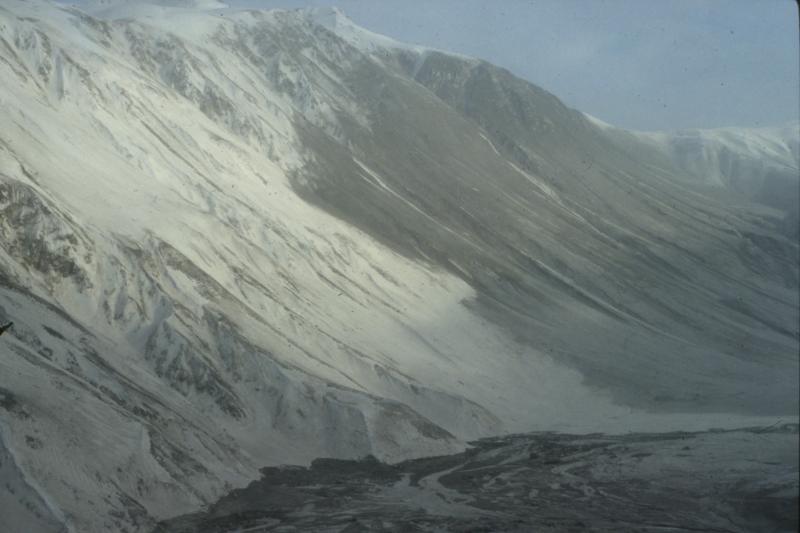 On February 15, 1990, collapse of the 2nd largest lava dome of the 1989-90 eruption of Redoubt Volcano generated a large pyroclastic flow and surge that swept north across the piedmont lobe of Drift Glacier and up and over the adjacent ridge (nicknamed Ptarmigan Ridge for a dead ptarmigan found on top).  This image shows deposits from the surge that traveled up and over the ridge.  Redoubt volcano is located off the image to the right.