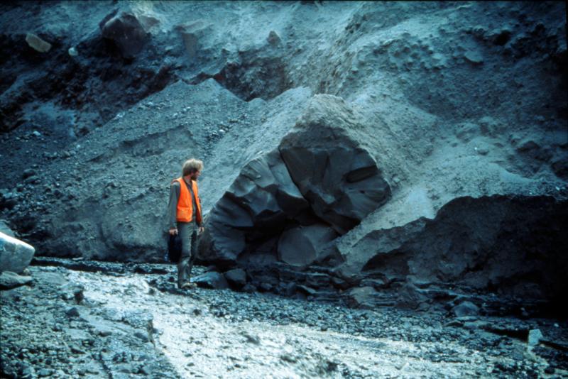 Game McGimsey examining prismatically jointed dome block in a pyroclastic deposit in upper Drift River valley from the 1989-90 eruption of Redoubt Volcano.


