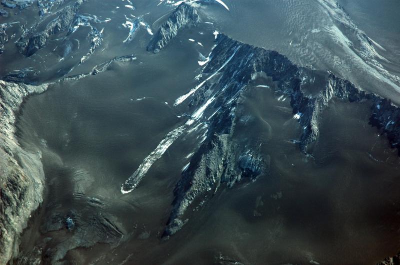 Recent avalanches showing the extent of the cumulative tephra deposit that blankets the area immediately north of Redoubt Volcano.  Summer snowmelt has coalesced the several tephra layers into one that now covers the glaciers and snowfields.				