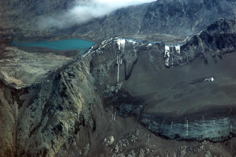 				Recent avalanches and rockfall showing the extent of the cumulative tephra deposit that blankets the area immediately north of Redoubt Volcano.  Summer snowmelt has coalesced the several tephra layers into one that now covers the glaciers and snowfields.				