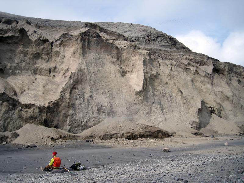 Thick sequence of Kasatochi 2008 deposits exposed along east-northeast coast. By August 2009 the sea cliff had retreated to expose bedrock of pre-eruption sea cliff (see image 19096). Lower massive to faintly bedded, yellowish-gray pyroclastic flow deposits are dry, friable and failing in slides, topples, and slumps. Pre-2008 lava flow exposed on skyline.