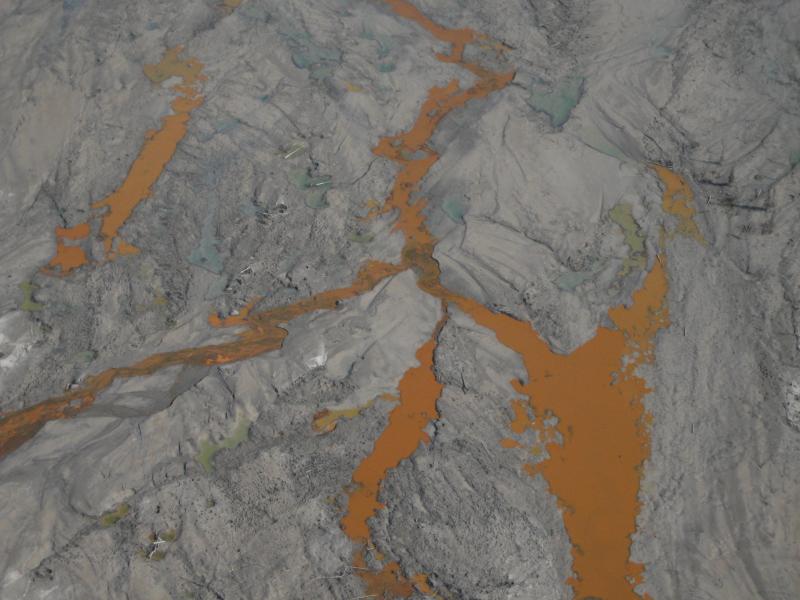 Naturally occurring groundwater seeps, rich in iron oxides, discolor channels in 2009 lahar deposits in the lower Drift River floodplain.   **AVO research technician Max Kaufman took these images during 3 days of campaign GPS work on and around Redoubt volcano: June 6,8,10 2009.