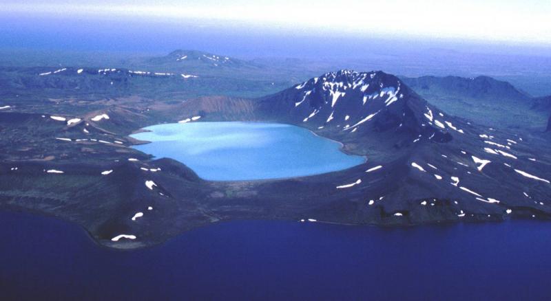 Turquoise cone, looking to the south.  In the foreground is the western caldera lake, and the snow-crested ridge in the middle distance is the southern caldera rim.  The collapse of Turquoise Cone removed more than half of the original stratocone, based on extrapolation of deposits in the existing edifice.  