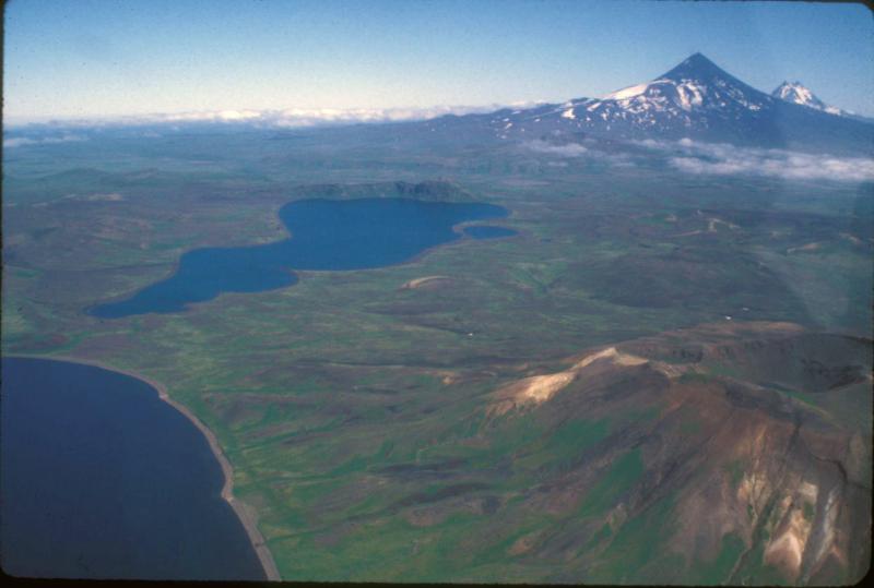 Looking northeast over most of Fisher caldera.  Mt. Finch, the most recently active vent at Fisher, is in the foreground on the right.  The lake in the foreground is the western caldera lake; the lake in the middle ground is the east caldera lake, and the cliff at the far end of this lake is the eastern caldera wall.  Shishaldin and Isanotski volcanoes in the background (right and far right, respectively).