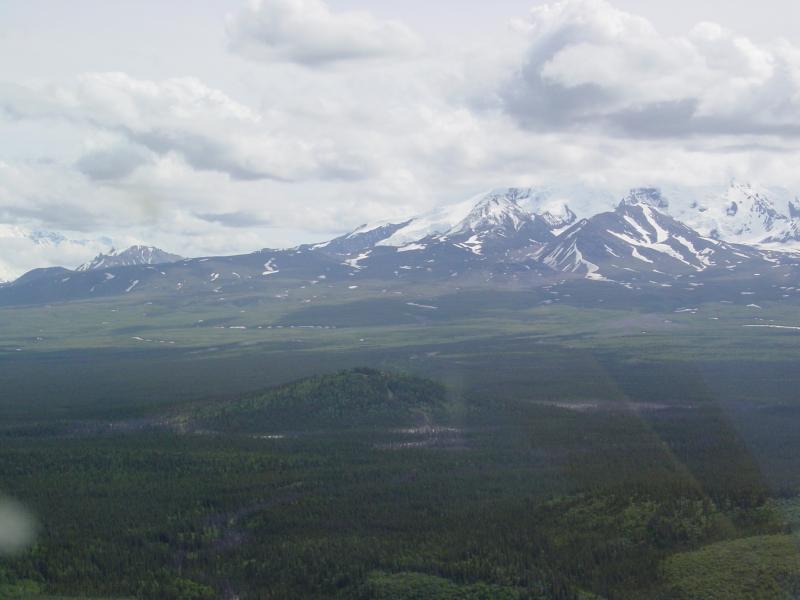 Aerial view from the west of Shrub mud volcano.  Shrub stands about 100 meters high above the Copper River basin.  The first eruption in historic times began in 1997 and continues (as of 2009, last USGS visit).  Mt. Drum in distance.
