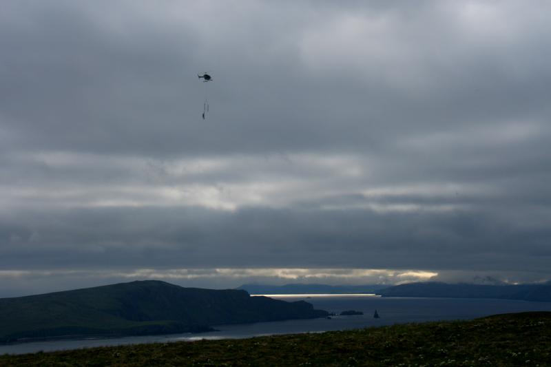 Helicopter pilot Chris Dean delivers a sling load of concrete and a solar panel 'swingset' to a new seismic installation on the east side of Akutan.