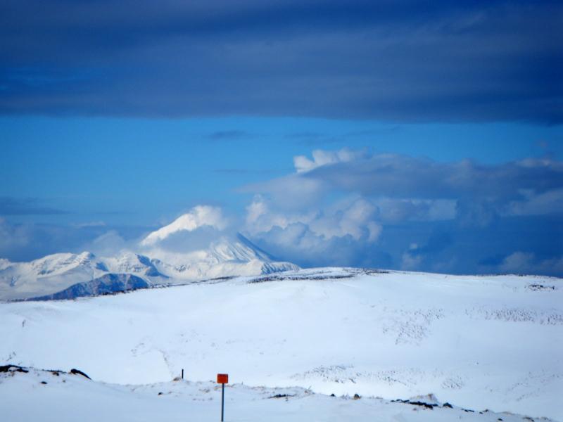 Kanaga Volcano issuing a steam plume.  Also visible is what appears to be two dark stripes extending down the flank (ash and/or flowage deposits?) that appear to be separate from the shadows.  Photo taken from the White Alice site, about 2 miles west of Adak, AK.