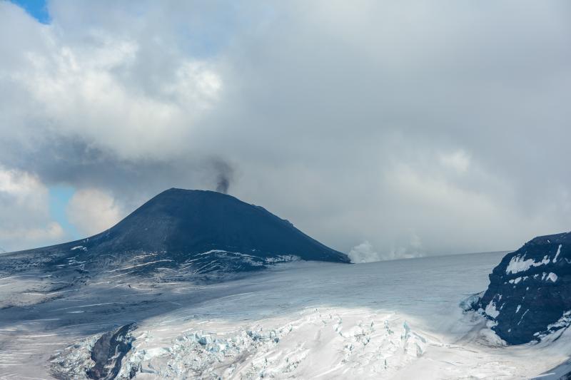 Low-level ash emission at the intracaldera cone of Veniaminof Volcano. Steaming area at the base of the cone to the right is the result of lava flowing over and resting on snow and ice. View is toward the southeast. 