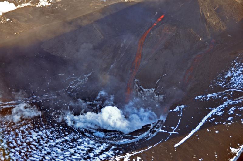 Veniaminof volcano in eruption, August 18, 2013.  A steady stream of molten lava flows down the east flank of the intracaldera cinder cone, advancing into an ice cauldron to produce a roiling steam plume. Photo taken by Game McGimsey, AVO/USGS. This overflight of Veniaminof was co-sponsored by the National Geographic Society.