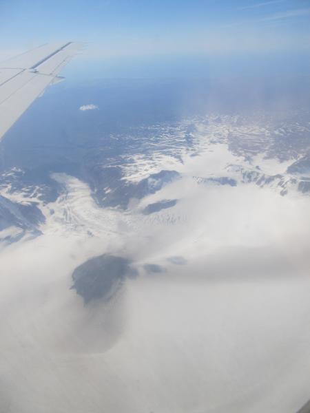View of Veniaminof volcano from a commercial flight to Sand Point, Alaska, on June 17, 2013.  Note the rays of darkened snow radiating away from the active intracaldera cinder and spatter cone; these were produced by ash fall from small and diffuse eruption clouds trailing downwind from the cone.  View is to the northwest; Cone Glacier (tongue of ice above the dark cone) descends from the summit caldera towards the Bering Sea coastline.