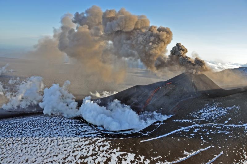 Veniaminof volcano in eruption, August 18, 2013.  Pulses of ash and ballistics erupt from the intracadera cinder cone.  Two streams of lava flow down the east flank into an ice cauldron to produce roiling steam clouds.  The lava flows are pouring from vents located below the crater rim, the highest (left in this image) of which likely marks the level of a lava lake within the cone. Photo taken by Game McGimsey, AVO/USGS. This overflight of Veniaminof was co-sponsored by the National Geographic Society.
