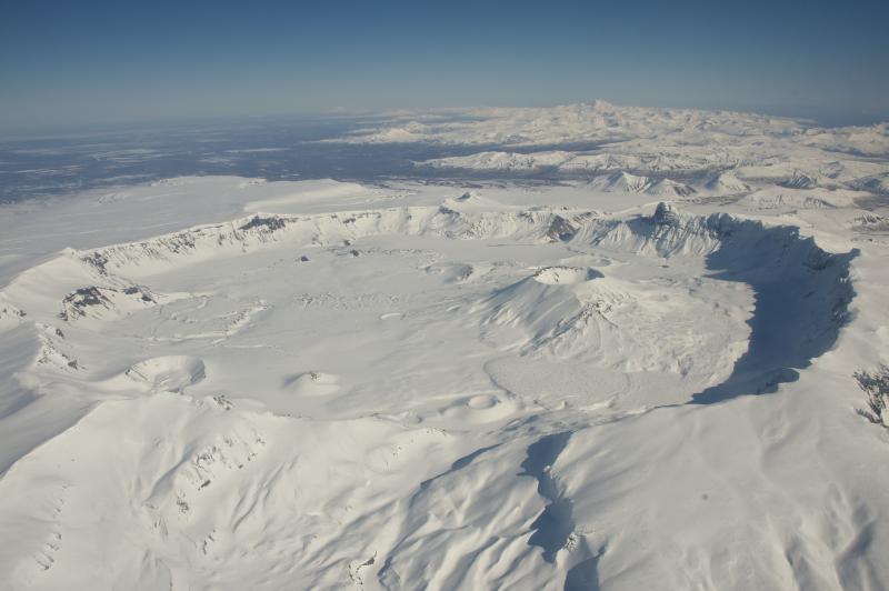 Aerial view of snow-covered, 6-mile-wide, Aniakchak Caldera on the Alaska Peninsula.  View is towards the northeast. Aniakchak last erupted in 1931. Chiginagak Volcano is the high peak on the horizon. Photo courtesy of Roy Wood, NPS.