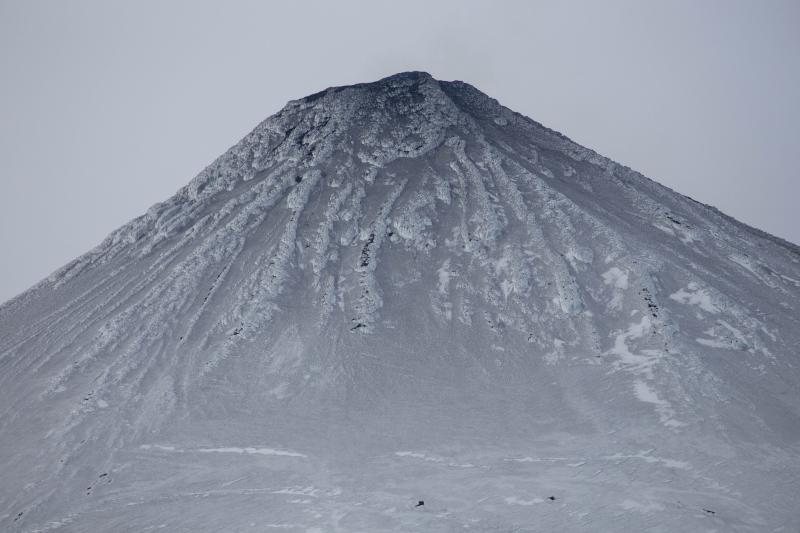 View of Shishaldin from AVO geophysical monitoring site SSLS southwest of the volcano, on June 28, 2014.    The upper flanks of the volcano are darkened by ash erupted over the last several months during low-level lava fountaining and small explosions deep in the summit crater.  On some days, a plume of steam and gas can be seen in the AVO web camera images. 