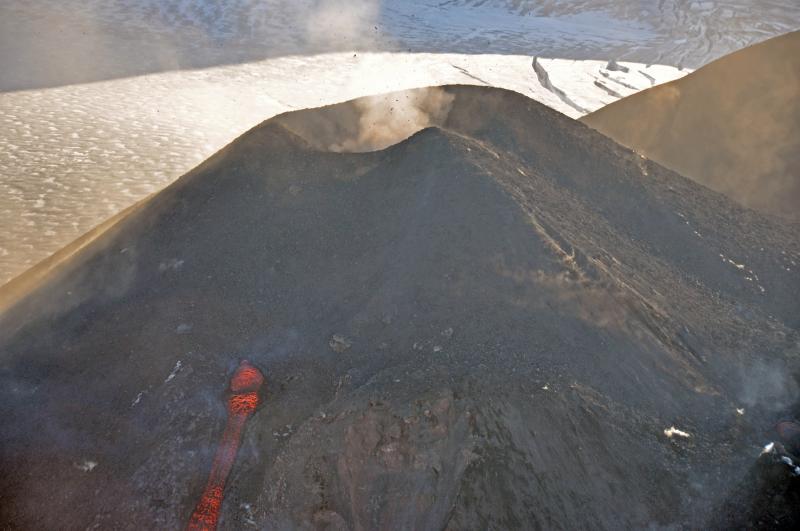 Erupting intracaldera cinder cone of Veniaminof volcano.   Lava bombs are being hurled from the  summit crater as lava pours from a vent on the upper flank feeding a flow that advances down to the ice filled caldera floor.