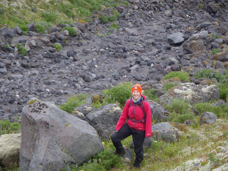 Geology student Anne Fulton stands adjacent to a recently active lahar channel on the north flank of Cleveland volcano.  Photo taken during the 2014 field season of the Islands of Four Mountains multidisciplinary project, work funded by the National Science Foundation, the USGS/AVO, and the Keck Geology Consortium.