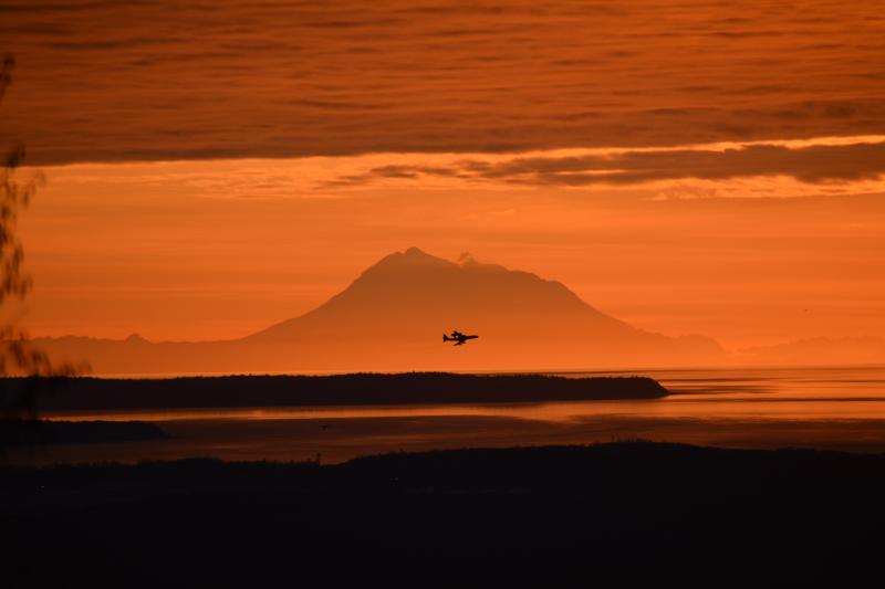 Redoubt volcano at sunset.  Just to the right of the summit, a small steam plume is visible rising from the 2009 lava dome.  In the foreground, a jet is taking off from the Ted Stevens Int&#039;l Airport.
