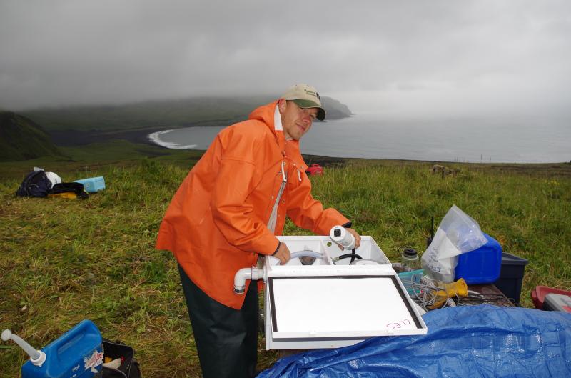 AVO&#039;s John Lyons working on installation of infrasound sensors at station CLES on th southeast flank of Cleveland volcano. South Cove in the distance. Photographs from the 2014 Islands of Four Mountains project. 