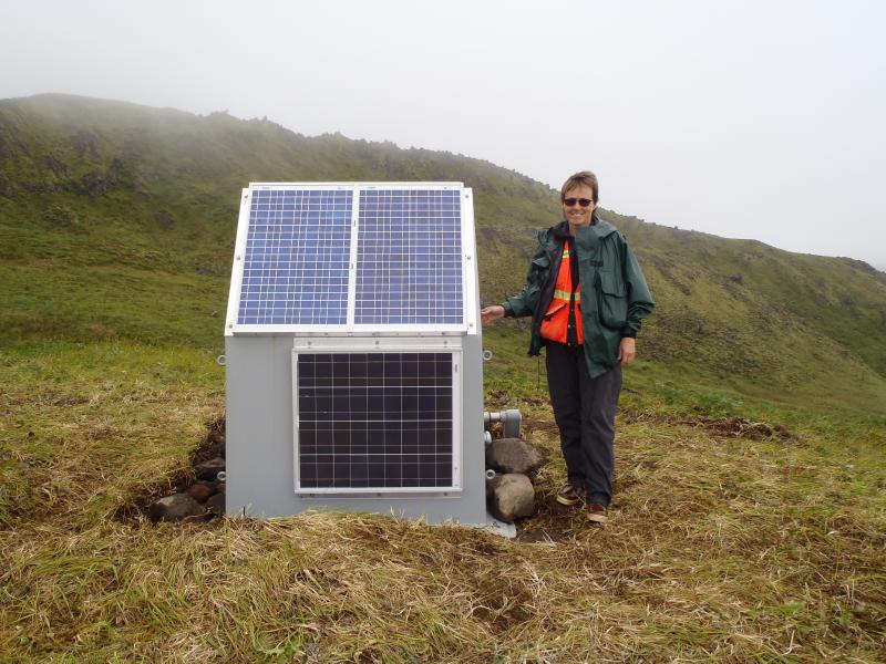 Tina Neal and station CLES enclosure, east flank Cleveland volcano. Photo taken during the 2014 field season of the Islands of Four Mountains multidisciplinary project, work funded by the National Science Foundation, the USGS/AVO, and the Keck Geology Consortium.