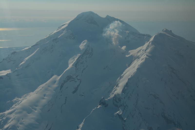 Aerial view from the north-northwest of the steaming lava dome in the summit crater of Redoubt Volcano.  The light bluish color of the steam cloud is indicative of gas (SO2).