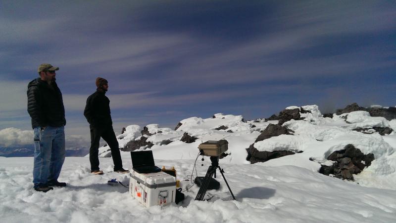 Gas measurement fieldwork on Augustine Volcano, June 7, 2015. Garth and Dane watching the camera measurements. Small clouds of condensed water can be seen coming off of the center of the dome.
