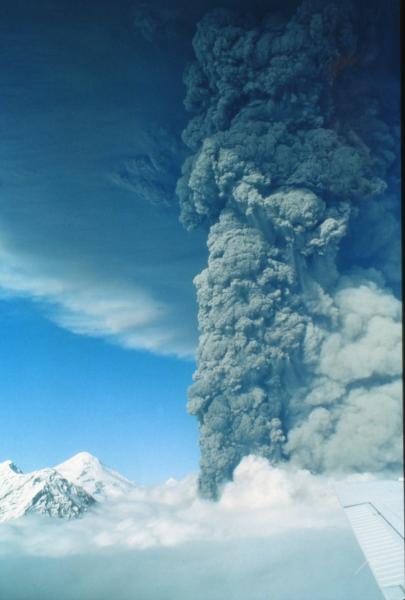Vertical eruption column and spreading ash cloud from eruption of Crater Peak satellite vent on Mount Spurr volcano.  The vent is several hundred feet below the top of the white clouds.  The lighter-colored, tan cloud to the right of the eruption column is fine ash rising from the pyroclastic flows that flowed down the east and southeast flank.  This view is to the north.  The summit of Mount Spurr (11,070 ft) is in the lower left corner, and about 2.2 miles north of Crater Peak.