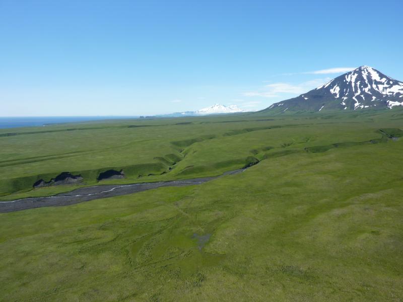 View to south from the northeast side of Umnak Island showing Recheshnoi and Vsevidof volcanoes to the far south and Mt. Tulik in the foreground.  The flat green terraces near Mt. Tulik are deposits from the 2050 BP caldera forming eruption of Okmok volcano.