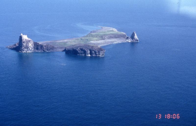 View from the northwest of Bogoslof Island.  Three lava domes of varying age are visible in the image.  To the far left is the 1992 dome; middle is the 1927 dome, and to the far right is Castle Peak (1796-1804).  The raised bench immediately left of Castle Peak is an accumulation of tephra deposits.