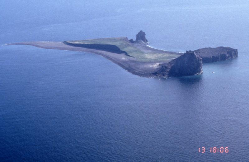 View from the northeast of Bogoslof Island.  Three lava domes are visible.  The closest (at north end of island) is the 1992 dome.  To the right (west) of it is the flat-topped 1927 dome. The farthest dome (midway along west shore) is Castle Peak, which was extruded during the 1796-1804 eruption.  The raised bench is an accumulation of tephra deposits.  Bogoslof is the emerged summit of a submarine stratovolcano that rises 6,000 feet from the Bering Sea floor.