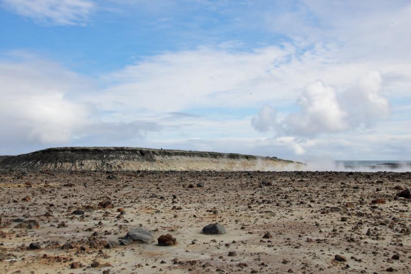 Day 1 of Bogoslof field work in August 2018. Former bay/lake bed facing south cliff of south northern shelf. Steam from fumaroles visible on right. Facing northeast.