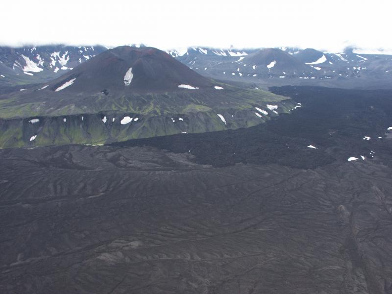 Cone D, Okmok caldera.  Cone A 1958 lava flow fills the foreground and the darker gray 1997 Cone A flow overtops the 1958 flow along the base of the Cone D bench.  Cone C is the next cone in the background to the right of Cone D.