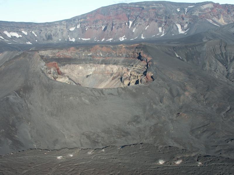 Multiple layers of volcaniclastics and lava flows are exposed in the crater wall of Cone E in Okmok volcano&#039;s caldera.  The 1997 Cone A lava flow is in the foreground at the base of Cone E.  The steep walls of Okmok caldera are seen on the skyline in the background.