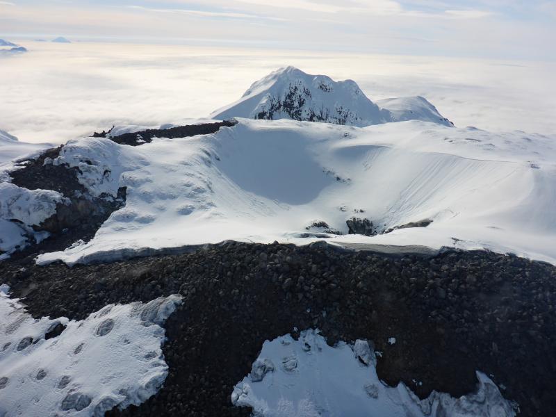 View of the summit dome at Great Sitkin during a gas flight. Very weak diffuse degassing observed all around the margins of the dome and also within the small crater on top. View is roughly to the west. Kanaga volcano is visible in the distance in the upper left.