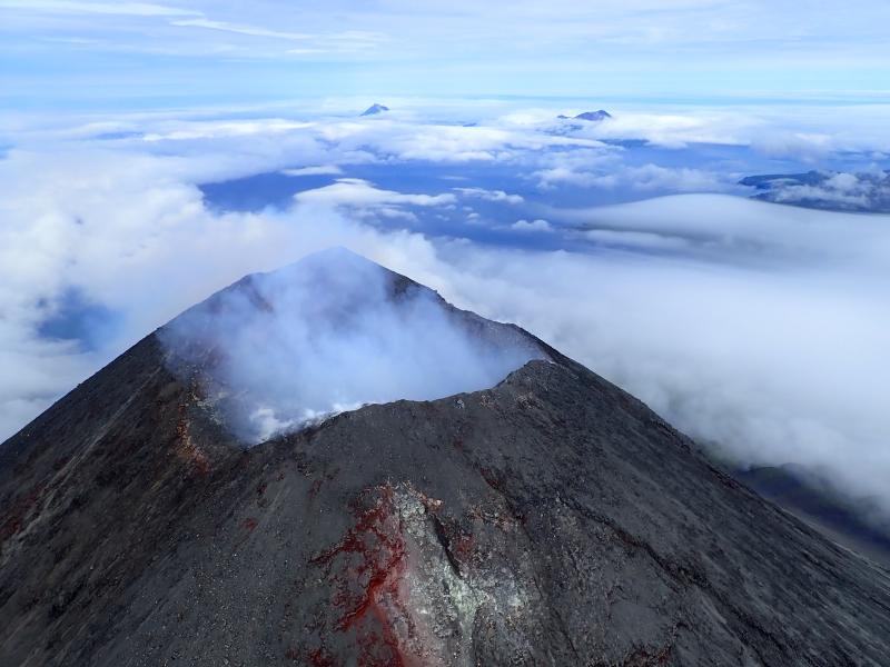 Summit of Cleveland Volcano,  in the Islands of Four Mountains group of the Aleutian chain.  Mild degassing from the summit vent obscures the crater and the plume drifts lazily off to the NNW. Islands in the background (L to R):  Uliaga, Kagamil, and the east half of Chuginadak.