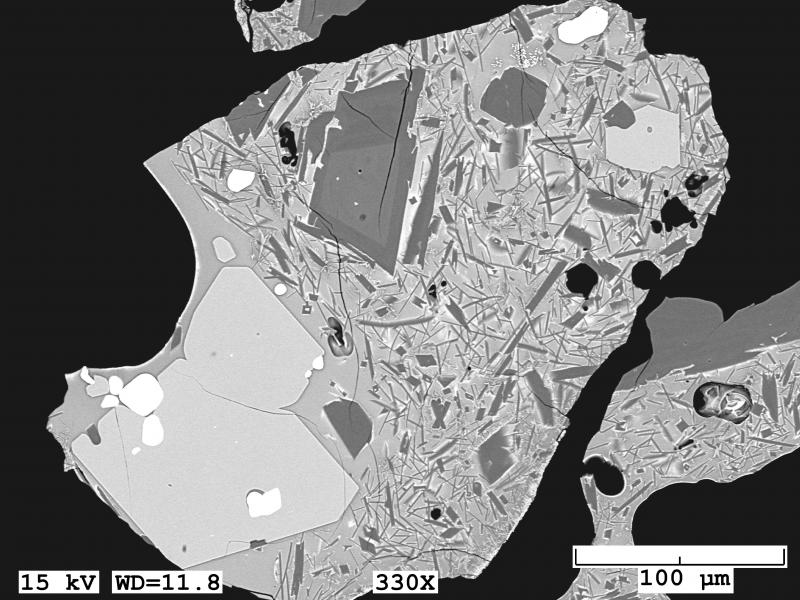 Backscattered electron image of tephra sample erupted from Shishaldin tephra erupted April 19, 1999. Dark gray crystals are plagioclase, light gray olivine, and white are Fe-Ti oxides. This imaged grain has a clean glassy matrix mixed with highly elongate plagioclase microlites. Image taken with a JEOL 6510LV Scanning Electron Microscope.