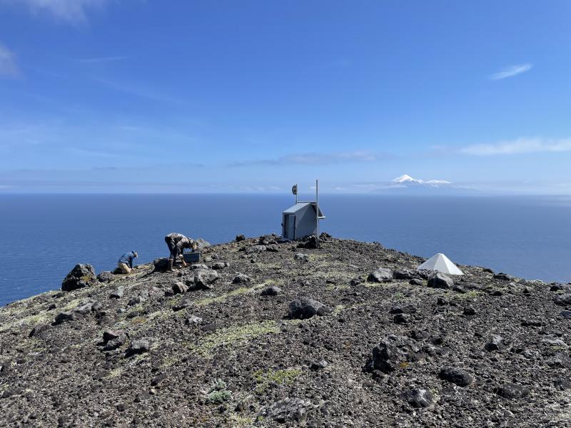 AVO field team replacing a failed seismometer on Gareloi Volcano, Andreanof Islands, western Aleutians.  Tanaga Volcano is visible in the distance.  