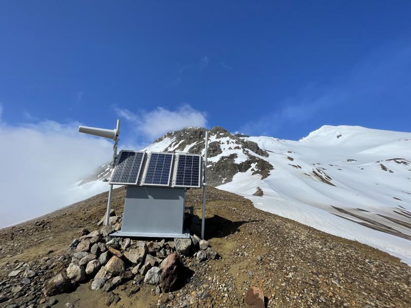 AVO field staff repairing site GSTD on Great Sitkin Volcano.  The new lava dome is just peeking out on the skyline.