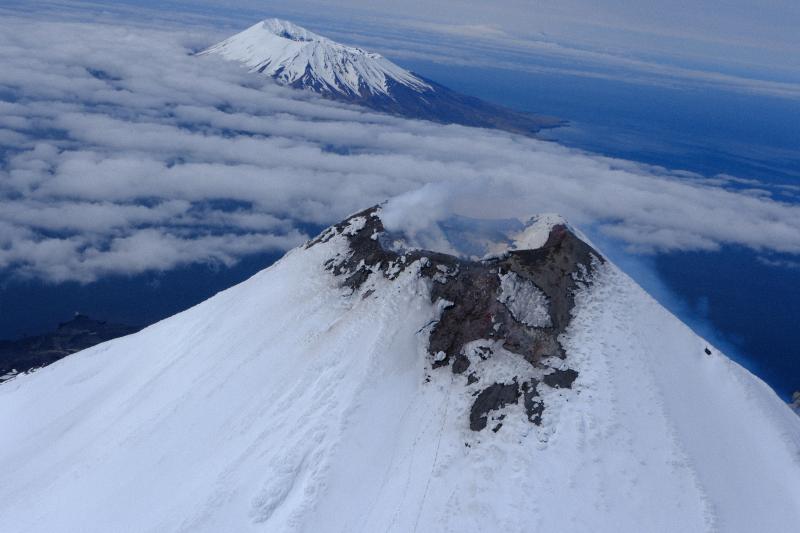 The summit of Cleveland Volcano on June 1, 2023, showing steaming and degassing at the summit crater. Herbert Island and cloud-covered Yunaska Island are visible in the background.