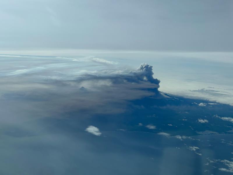 Eruptive plumes from the August 4, 2023, eruption of Shishaldin Volcano taken by a passing aircraft flying at 31,000 ft. The view is from the north and shows the higher, white and puffy gas-rich plume, the lower, gray ash-rich plume, and proximal dark tephra deposits on the volcano&#039;s flank. The summit of Isantoski is also visible through the plume and meteorological clouds.