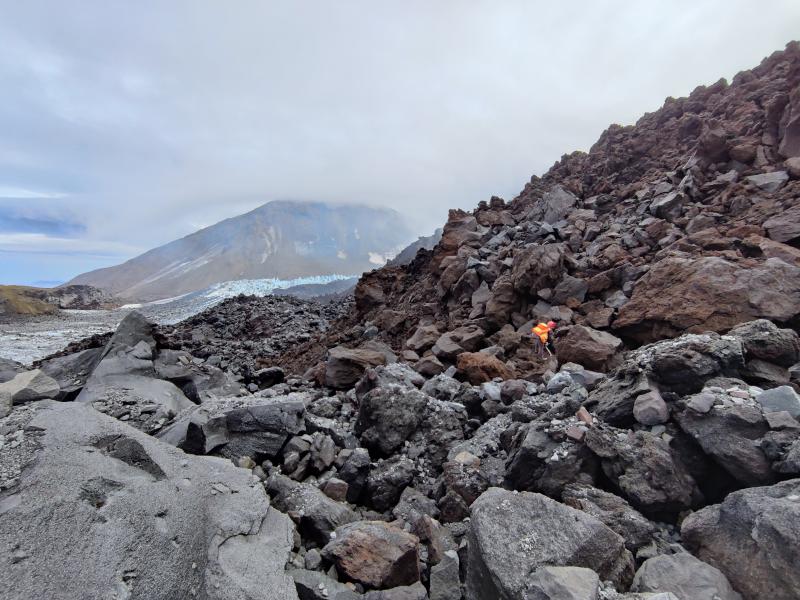 AVO personnel collect a sample from the ongoing eruption of lava in the summit crater of Great Sitkin Volcano during fieldwork in summer 2023.