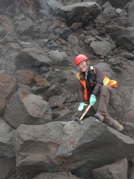 AVO personnel collect a sample from the lava flow of the eruption continuing in 2023 within the summit crater of Great Sitkin Volcano during fieldwork in the central Aleutians.