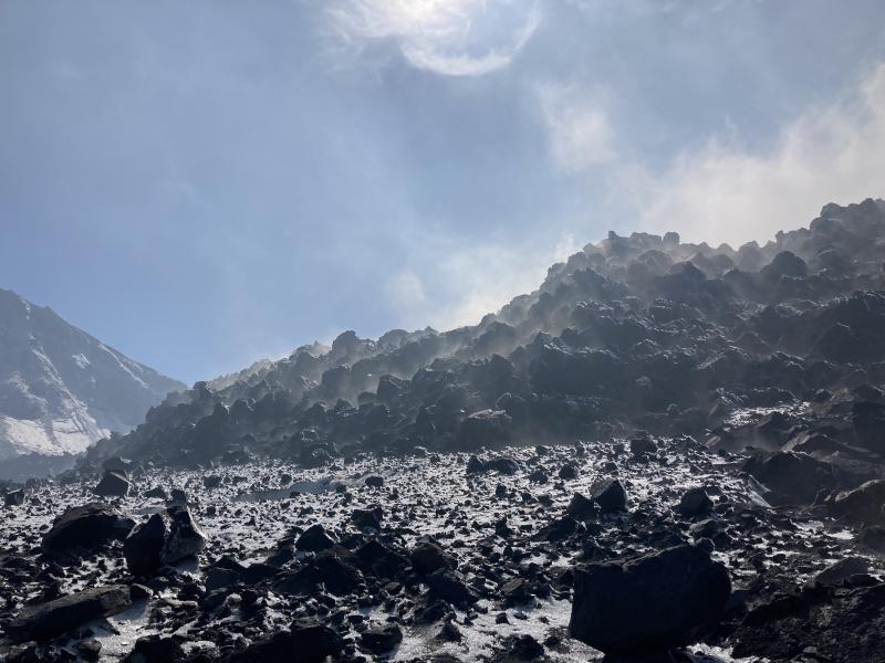 The 2021-2023 lava flow in the summit crater of Great Sitkin Volcano steams on September 1, 2023, during at sampling visit by AVO geologists. The blocks on the intracrater glacier in the foreground were blasted out during the May 25, 2021 eruption.