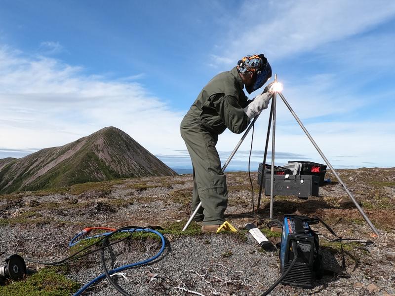 Installation of AVO&#039;s new seismic and GNSS network at Mt. Edgecumbe volcano, August 20-29 2023.  AVO field technician Max Kaufman constructs GNSS antenna monument at site EDCR on Crater Ridge. 12 ft long by 1&quot; stainless steel rods are driven 7 ft into the ground, and welded together at the top.