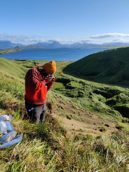 An AVO geologist takes photos of a tephra site on the south flank of Adagdak Volcano on Adak Island during fieldwork in the central Aleutians in summer 2023. The zip-top bags visible on the ground contain samples of tephra layers to be transported back to AVO for analysis.