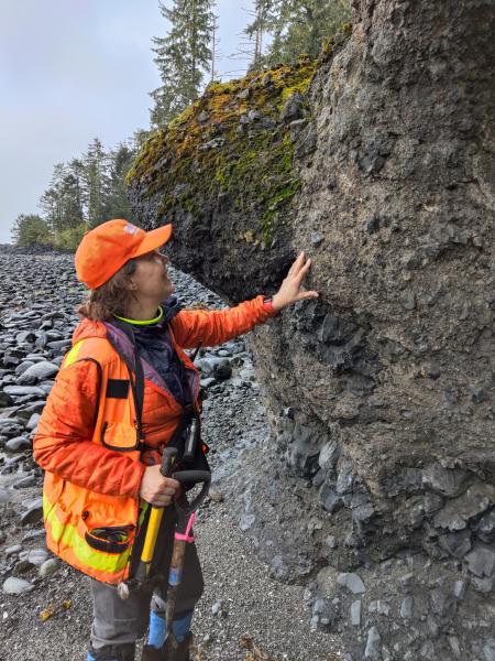 AVO/USGS geologist Michelle Coombs examines a lava pillar found on a beach on the east side of Kruzof Island. The lava is a hyaloclastite, meaning it contacted cold water while still hot, forming the distinctive texture seen here. Taken during fieldwork at Mount Edgecumbe, May 2024.