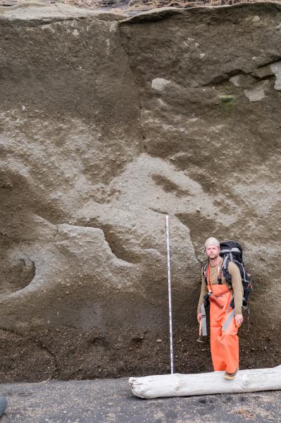 Over 5 m thick exposure of indurated pyroclastic density current deposits from the Fisher caldera forming eruption exposed on Cape Lapin north of Shishaldin Volcano, near site 24SHML03. Geologist Jordan Lubbers and a 2 m scale bar are at the base of the exposed section.