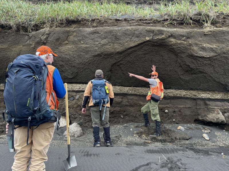 AVO geologist M. Loewen (right) discussing eruption dynamics of the Fisher caldera forming eruption with UAF geologist P. Izbekov (middle) and AVO geologist C. Waythomas (left). The ignimbrite from the Fisher caldera forming eruption is the top, thick unit M. Loewen is pointing at, and the airfall deposit associated with it is immediately below. This airfall is easily recognized by its black basal pumice and lighter cream colored pumice immediately on top.